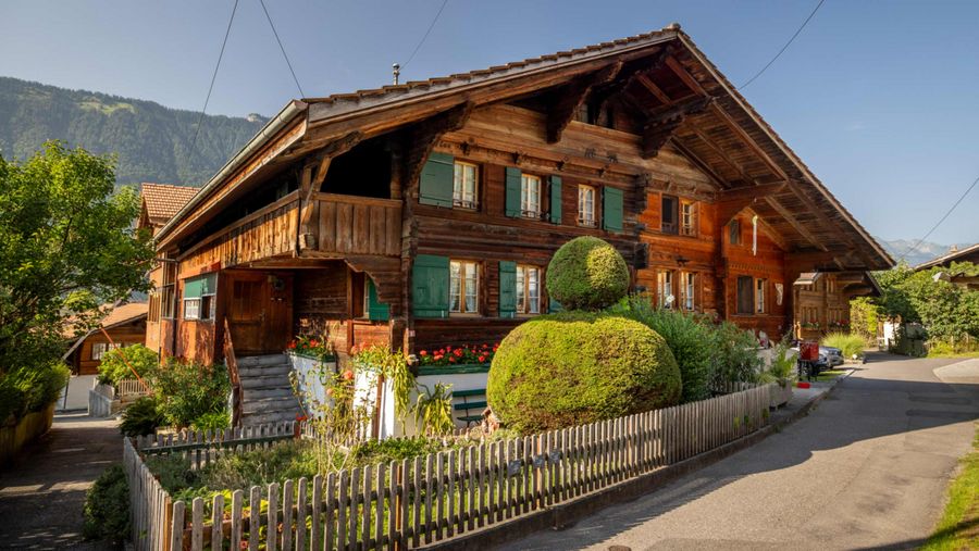 Holzhaus mit grünen Balken und Schnitzereien sowie schönen Geranien auf einem Dorfrundgang durch Bönigen