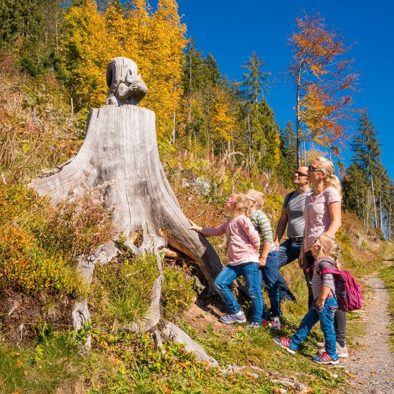 Familie wandert in Beatenberg und bestaunt die Holzskulptur am Wegrand