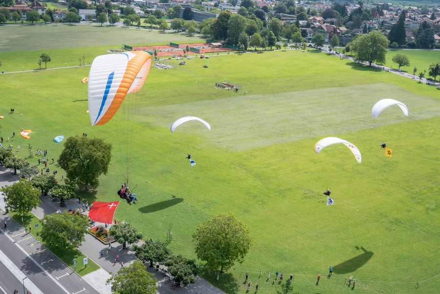 Paraglider mit Kanonsfahnen der Schweiz über der grünen Höhematte