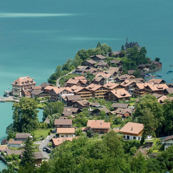 Das idyllische Fischerdorf Iseltwald aus der Vogelperspektive. Charmante Häuser und der smaragdgrüne Brienzersee sind zu sehen.